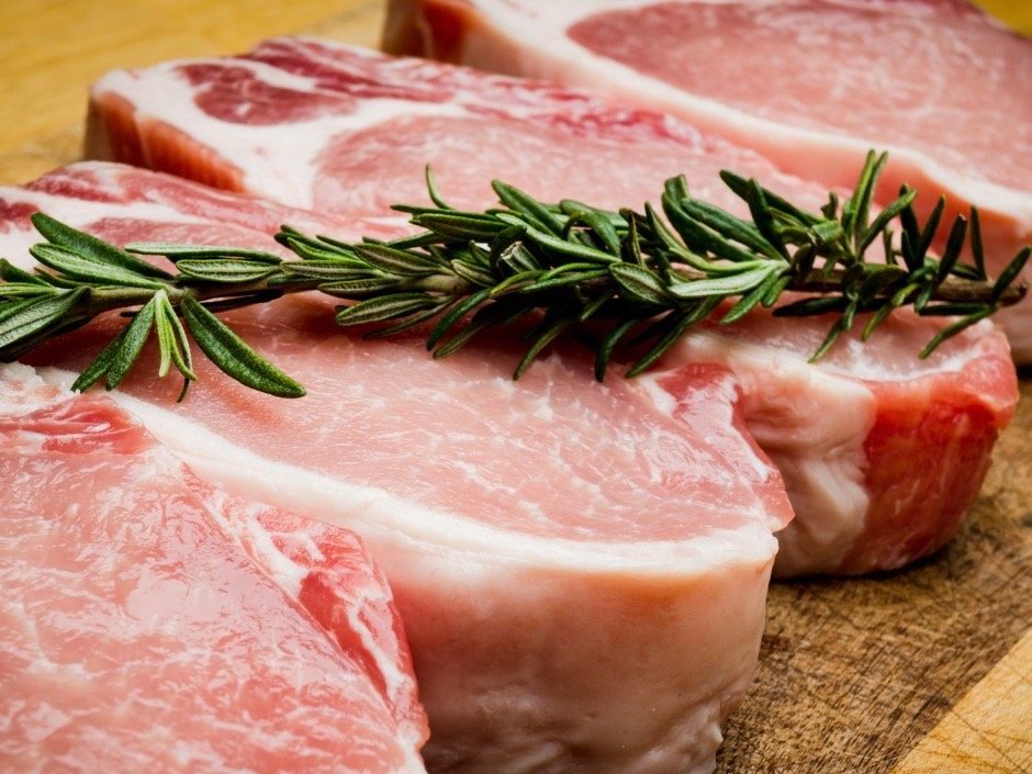 Fresh pork chops seasoned with sprigs of rosemary on a wooden cutting board, showcasing the marbling and texture of the meat.